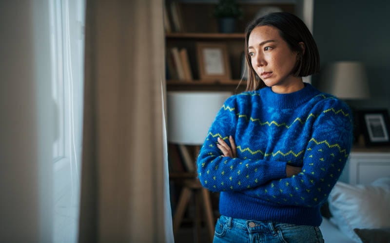 A young depression woman standing with her arms folded, and looking out the window.