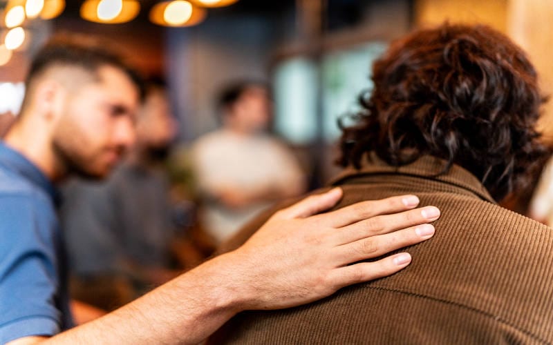 A man with his hand on another man's shoulder, telling him how untreated mental health conditions can lead to substance use.