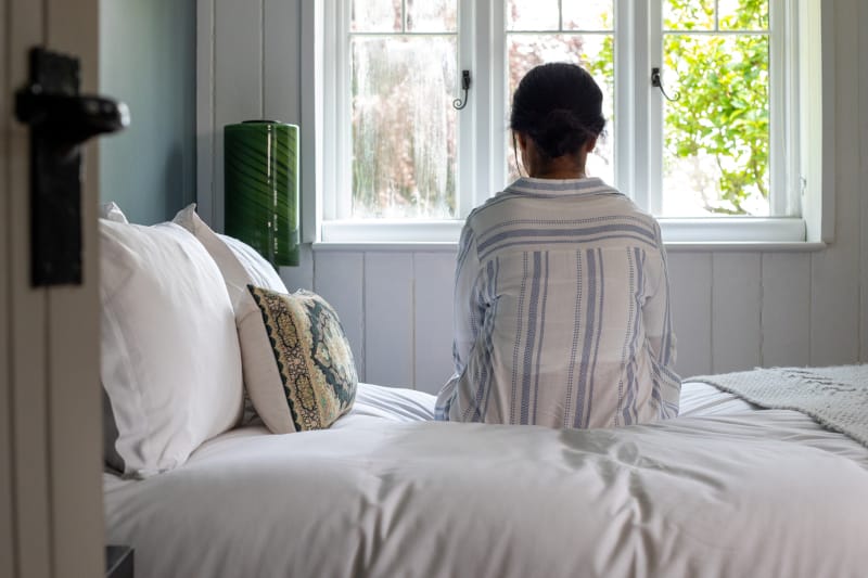 A person sitting on a bed debating whether they have bipolar disorder or depression.