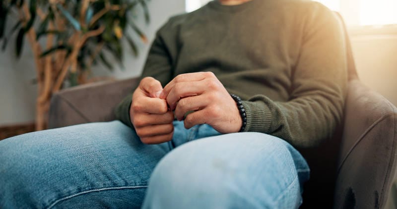 A picture of a man suffering from obsessive thoughts, or OCD, picking at his fingers.